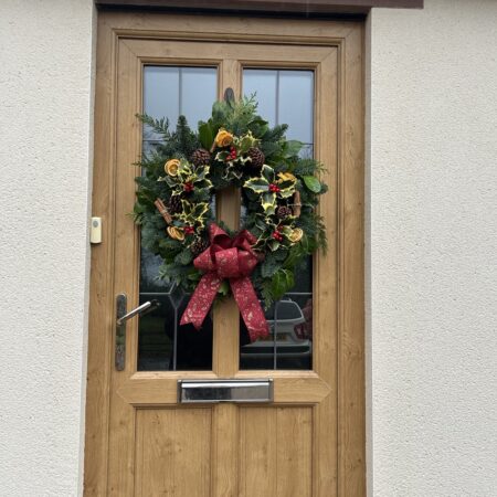 Festive Christmas wreath with holly, pine cones, dried orange slices and a red bow on a wooden door at Netherby Hall.